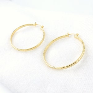 May include: A pair of gold hoop earrings with a textured design. The earrings are large and have a circular shape.