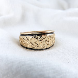 May include: A gold ring with a black band and intricate floral designs.