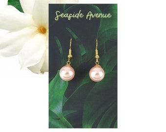 May include: A pair of gold dangle earrings with pink pearl drops. The earrings are displayed on a card with the text "Seaside Avenue".