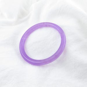 May include: A purple bangle bracelet made of jade. The bracelet is smooth and polished, with a subtle shimmer.