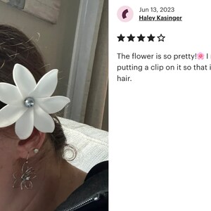 May include: A white flower hair clip with a pearl center. The flower is attached to a person's hair. The flower is so pretty! I might try putting a clip on it so that it stays in my hair.
