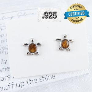 May include: Sterling silver turtle stud earrings with a brown and gold shell design. The earrings are marked .925, indicating they are made of sterling silver.