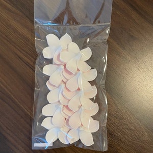 Puede incluir: Una bolsa de pl&aacute;stico transparente llena de p&eacute;talos de flores de tela de color rosa p&aacute;lido.
