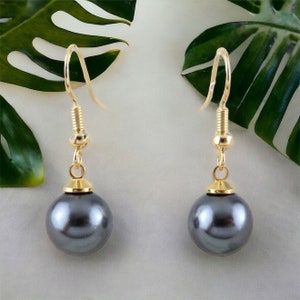 May include: A pair of gold dangle earrings with a dark gray pearl on each earring.