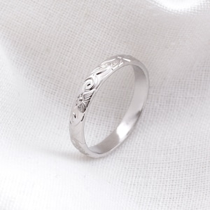 May include: A silver band ring with a floral design engraved around the band.