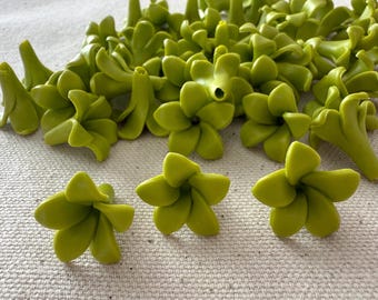 May include: A collection of small, light green, flower-shaped objects. The objects have multiple petals and a slightly textured appearance. The flowers are scattered across a neutral-colored surface, with some clustered together and others isolated.