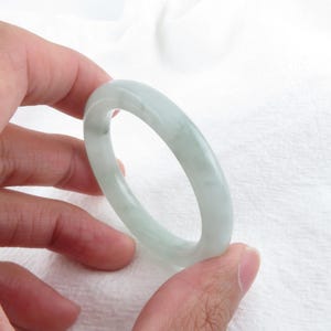 Pode incluir: Um bracelete de jade verde claro. O bracelete é liso e polido, com um brilho sutil.