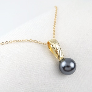 May include: A gold chain necklace with a black pearl pendant. The pendant features a floral design.