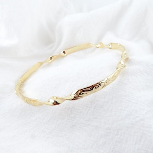 May include: A gold-toned twisted bangle bracelet with an engraved design.