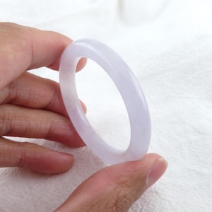 Könnte beinhalten: Ein helles, lavendelfarbenes Jade-Armband. Das Armband ist glatt und poliert, mit einem schlichten, eleganten Design.