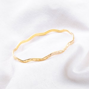 May include: A gold-toned, wavy bangle bracelet with a hammered texture.