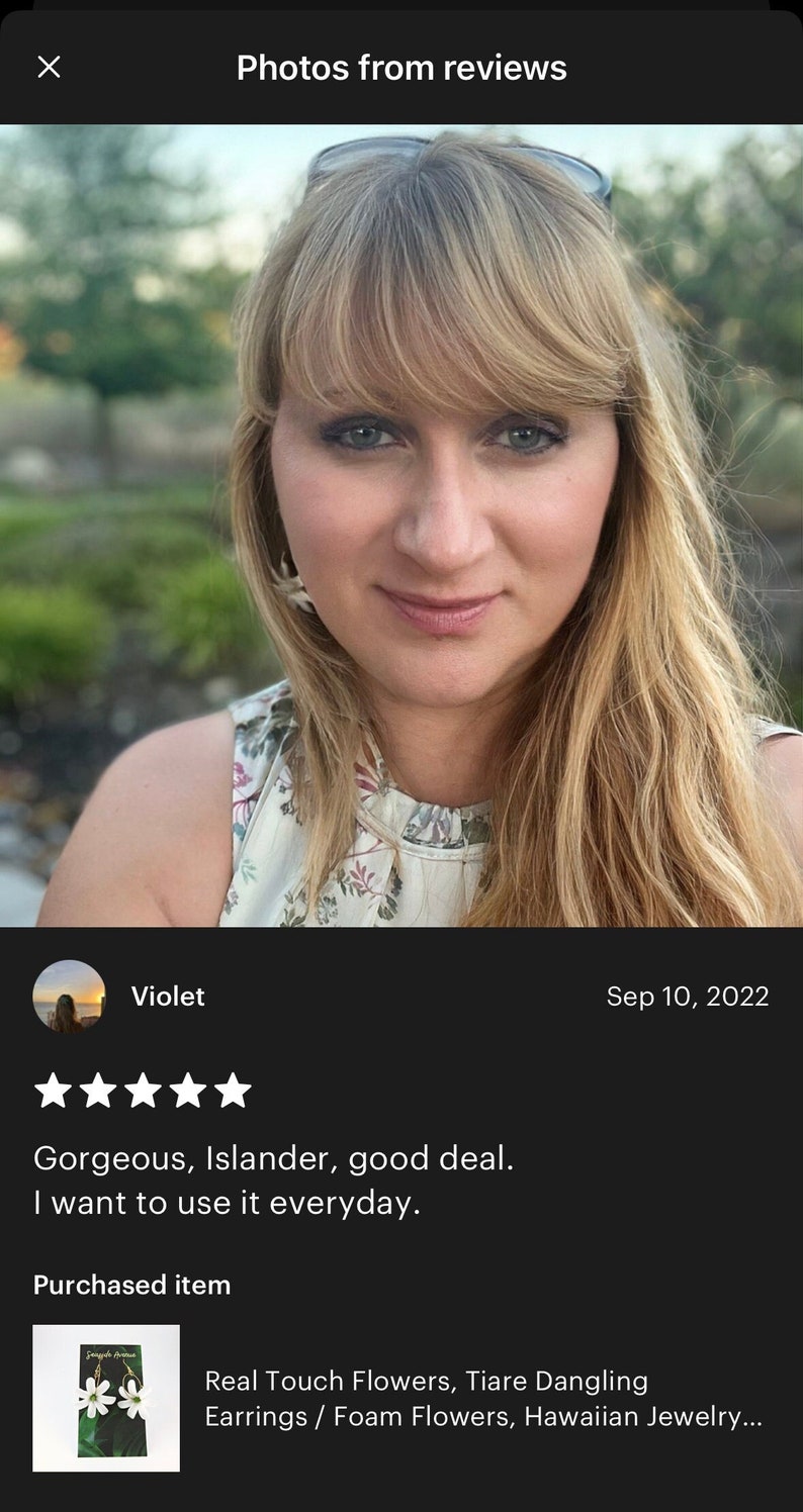 May include: A woman with blonde hair and blue eyes is smiling at the camera. She is wearing earrings with white flower designs. The image includes a review with the text "Gorgeous, Islander, good deal. I want to use it everyday."