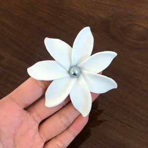 May include: A white flower with five petals and a silver bead in the center.