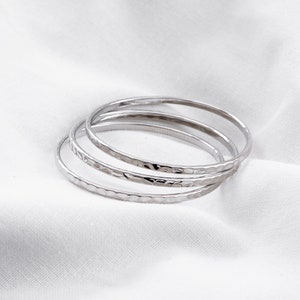 May include: Four silver hammered bangle bracelets stacked on top of each other. The bracelets are smooth and shiny.