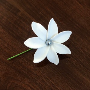 May include: A white flower with five petals and a silver bead in the center. The flower is attached to a green stem.