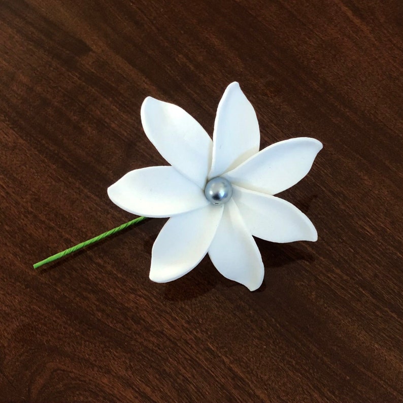 May include: A white flower with five petals and a silver bead in the center. The flower is attached to a green stem.