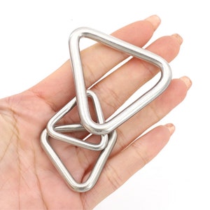 May include: Two silver triangle-shaped metal rings, one slightly smaller than the other, are stacked on top of each other. The rings are smooth and shiny.