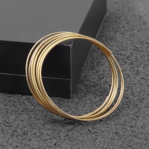 May include: A set of six gold-colored metal rings, stacked on top of each other. The rings are round and have a smooth, polished finish.