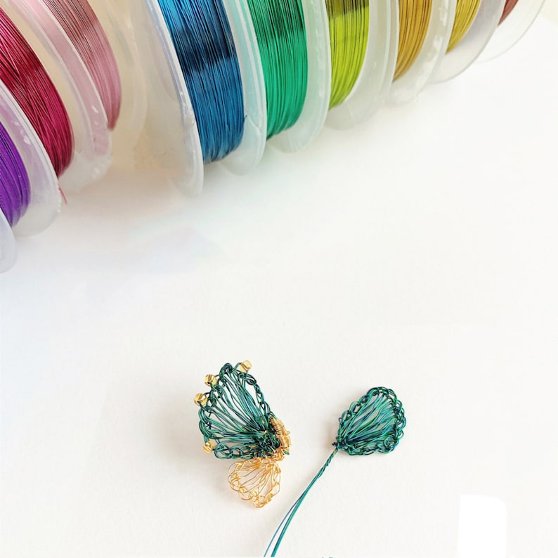 May include: Two green wire flower embellishments with gold accents. The embellishments are on a white surface.