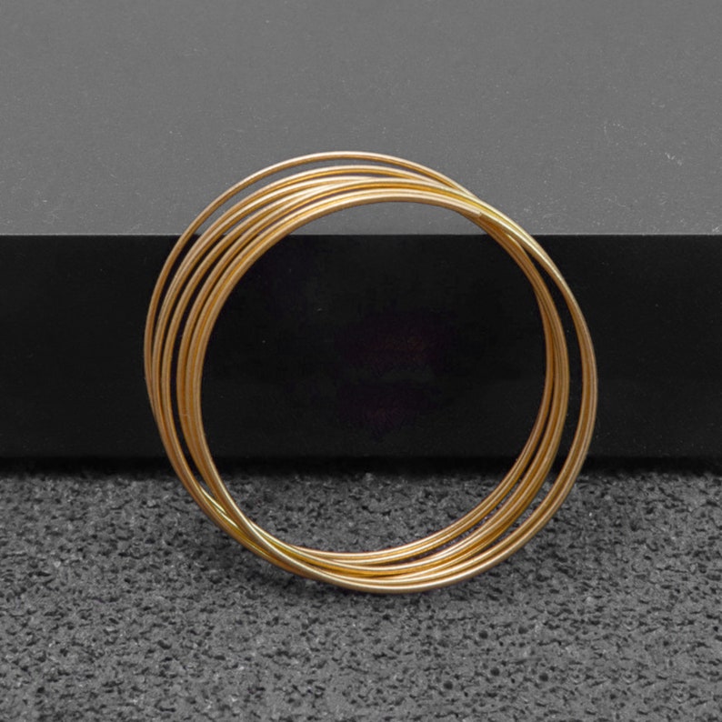 May include: A set of five gold-colored metal bangles stacked on top of each other.