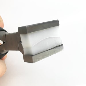 May include: Close-up of a silver jewelry pliers with white plastic jaws. The jaws are designed to crimp jewelry findings.