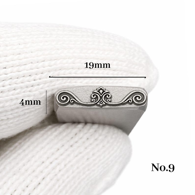 Op de afbeelding: Een metalen stempel met een sierlijk krulontwerp, 19 mm breed en 4 mm hoog. De stempel heeft een centraal decoratief element en is gemarkeerd met "No.9".