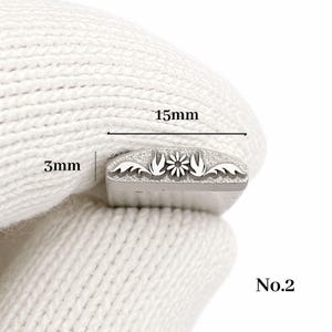 Op de afbeelding: Een metalen stempel met een bloemmotief, 15 mm lang en 3 mm hoog. De stempel heeft een centrale bloem geflankeerd door gestileerde bladeren. Het nummer "No.2" is rechtsonder zichtbaar.