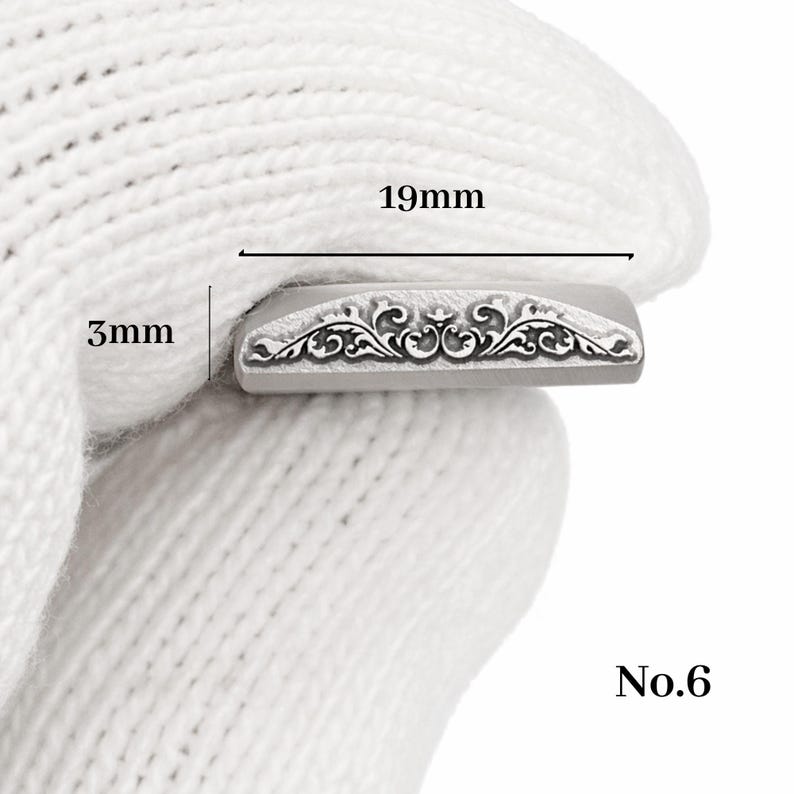 Op de afbeelding: Een kleine, rechthoekige metalen stempel met een sierlijk bloemmotief. De stempel is 1,9 cm lang en 3 mm breed. Het nummer "No.6" staat rechtsonder gedrukt.