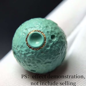 May include: A turquoise blue sphere with a gold rim around a small indentation. The sphere has a textured surface with small craters.