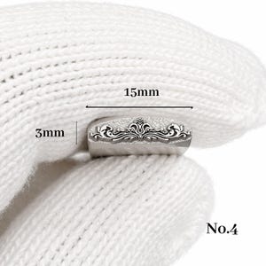 Op de afbeelding: Een kleine, zilverkleurige metalen stempel met een sierlijk bloemmotief. De stempel is 15 mm lang en 3 mm hoog. Het nummer "No.4" is zichtbaar. De stempel wordt in een witte handschoen gehouden.