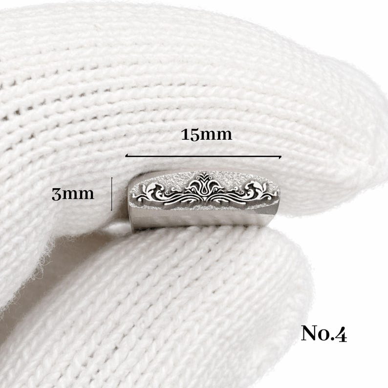 Op de afbeelding: Een kleine, zilverkleurige metalen stempel met een sierlijk bloemmotief. De stempel is 15 mm lang en 3 mm hoog. Het nummer "No.4" is zichtbaar. De stempel wordt in een witte handschoen gehouden.