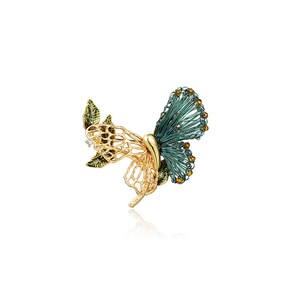 May include: A gold and green butterfly brooch with a delicate wire design. The butterfly has a green body and wings with gold accents and a clear rhinestone.