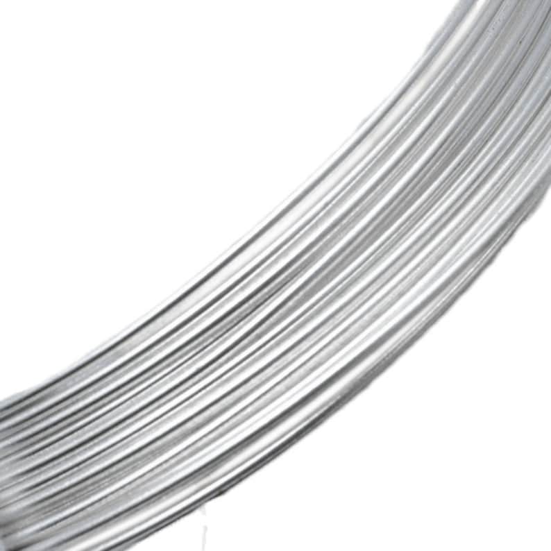 May include: Close-up of a bundle of shiny, silver-colored wire. The wire is tightly wound, creating a curved shape against a white background. The texture of the wire is smooth and reflective, suggesting a metallic material.