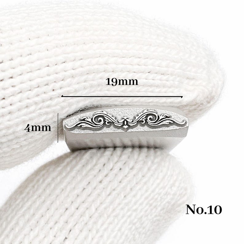Op de afbeelding: Een metalen stempel met een sierlijk, symmetrisch ontwerp, 1,9 cm lang en 0,4 cm breed. De stempel heeft een decoratief krulpatroon. Het nummer "No.10" staat rechtsonder afgedrukt.