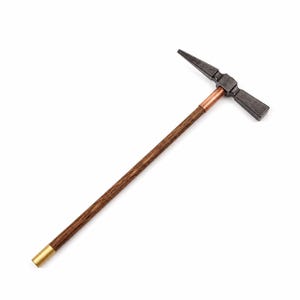May include: A geological hammer featuring a dark metallic head with a pointed pick and a flat face. The handle is made of brown wood with a visible grain, accented by a copper-colored ferrule near the head and a brass-colored cap at the base.