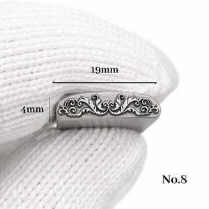 Op de afbeelding: Een zilveren metalen stempel met een sierlijk bloemmotief, 19 mm lang en 4 mm hoog. De stempel wordt in een witte handschoen gehouden. Het nummer "No.8" is rechtsonder zichtbaar.