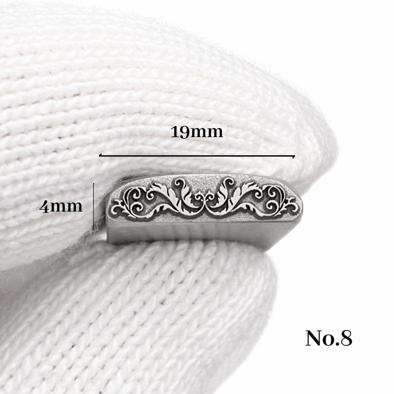 Op de afbeelding: Een zilveren metalen stempel met een sierlijk bloemmotief, 19 mm lang en 4 mm hoog. De stempel wordt in een witte handschoen gehouden. Het nummer "No.8" is rechtsonder zichtbaar.