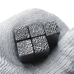 Puede incluir: Cuatro pequeños bloques de metal cuadrados con diferentes superficies texturizadas. Los bloques están dispuestos en una cuadrícula de 2x2.