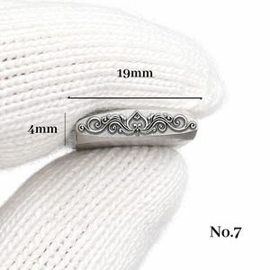 Op de afbeelding: Een zilverkleurig, rechthoekig metalen object met een sierlijk, symmetrisch ontwerp. Het object is 19 mm lang en 4 mm breed. De tekst "No.7" is rechtsonder zichtbaar.