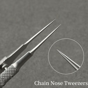 K&ouml;nnte beinhalten: Nahaufnahme einer Spitzzange, ein Pr&auml;zisionswerkzeug mit langen, spitzen Spitzen. Das Metallwerkzeug hat einen strukturierten Griff f&uuml;r besseren Halt und ist f&uuml;r Detailarbeiten konzipiert. Der Text "Chain Nose Tweezers" wird unten angezeigt.