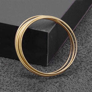 May include: A set of four gold-toned metal bangles stacked together. The bangles are smooth and shiny.