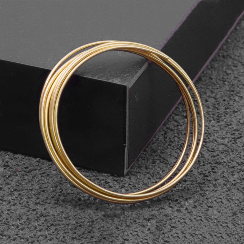 May include: A set of four gold-toned metal bangles stacked together. The bangles are smooth and shiny.