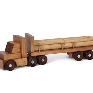 Pu&ograve; includere: Un camion giocattolo di legno con un rimorchio a pianale che trasporta tronchi. Il camion &egrave; marrone e ha ruote nere. I tronchi sono di colore marrone chiaro e sono impilati uno sopra l'altro.