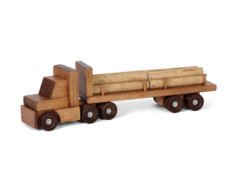 Pu&ograve; includere: Un camion giocattolo di legno con un rimorchio a pianale che trasporta tronchi. Il camion &egrave; marrone e ha ruote nere. I tronchi sono di colore marrone chiaro e sono impilati uno sopra l'altro.