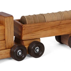 Pu&ograve; includere: Un camion giocattolo di legno con un rimorchio che trasporta tronchi. Il camion &egrave; marrone e ha ruote nere. Il rimorchio &egrave; anche marrone e ha ruote nere. I tronchi sono marroni e sono impilati nel rimorchio.