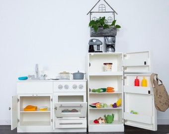May include: White toy kitchen playset with a stove, oven, refrigerator, and cabinets. The refrigerator has shelves and a door that opens. The stove has a black oven door and four knobs. The cabinets have shelves and doors that open. The playset is made of wood and has a white finish.