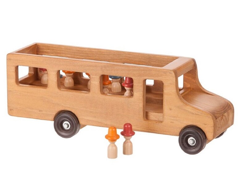 May include: A wooden toy bus with a brown finish and open windows. The bus has a driver's seat and a row of seats for passengers. There are small wooden figures with colorful hats standing in front of the bus.