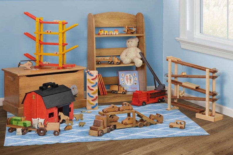 May include: A wooden toy playroom with a red toy barn, a wooden toy truck carrying smaller toy cars, a wooden toy fire truck, a wooden toy helicopter, a wooden toy train, a wooden toy spiral, a wooden toy shelf with a teddy bear, a wooden toy ramp, and a wooden toy chest.
