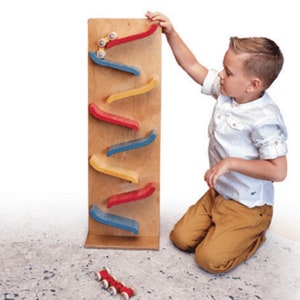 May include: A wooden toy with colorful ramps for rolling toy cars down. A child is playing with the toy, which is standing on a rug.