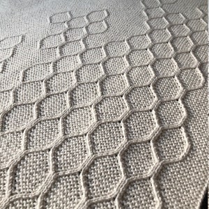 Puede incluir: Una manta de punto beige con un patr&oacute;n geom&eacute;trico de panal.